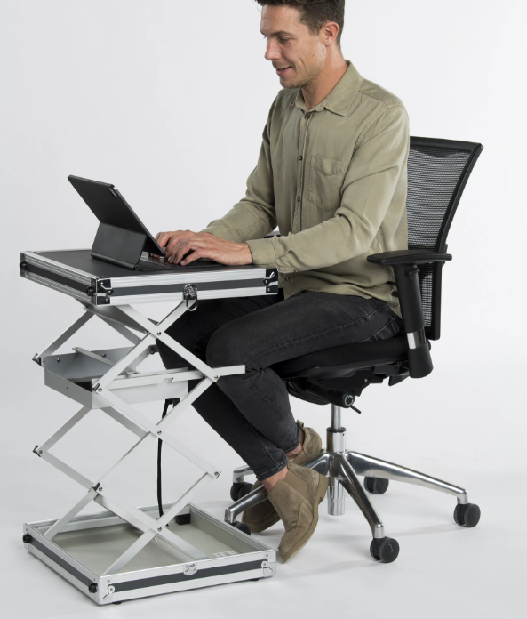 Man zit op een bureaustoel en werkt op een tablet op een in hoogte verstelbare, opvouwbare werktafel tegen een witte achtergrond.