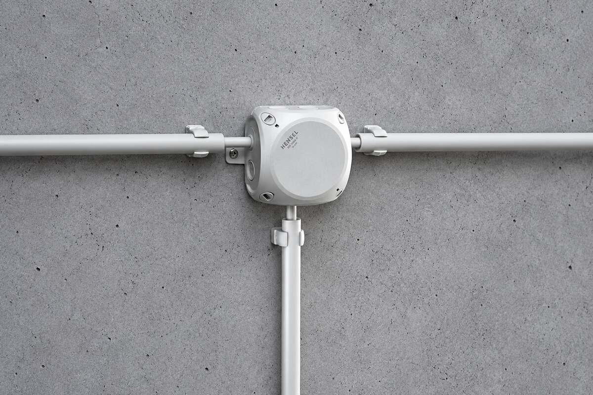Grijze aftakdoos met installatiebuizen op een betonnen wand